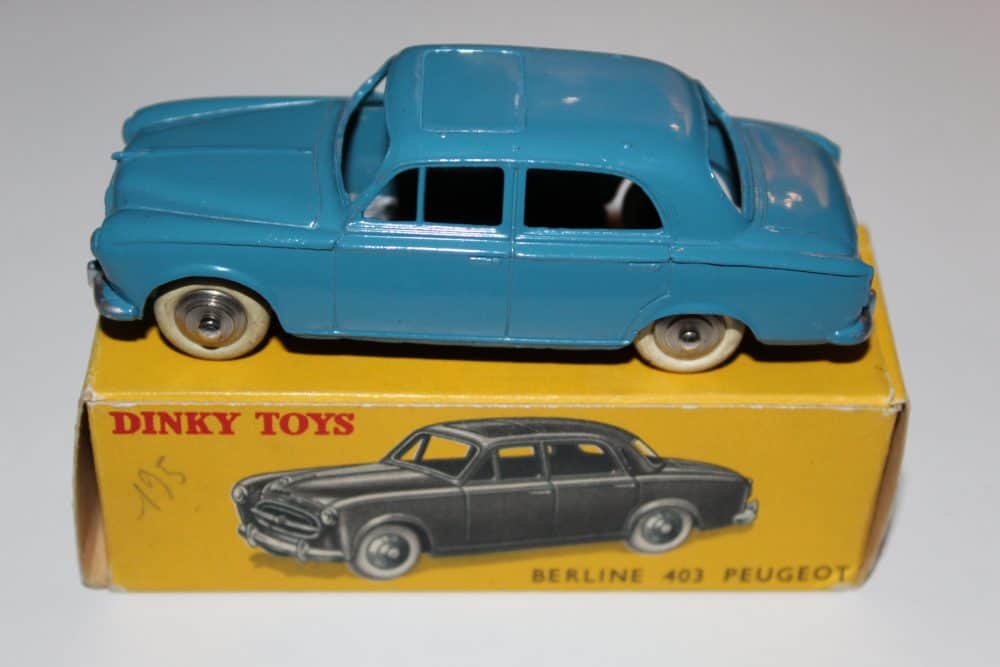 Vintage blue Dinky Toys Peugeot 403 Berline diecast car on yellow box.