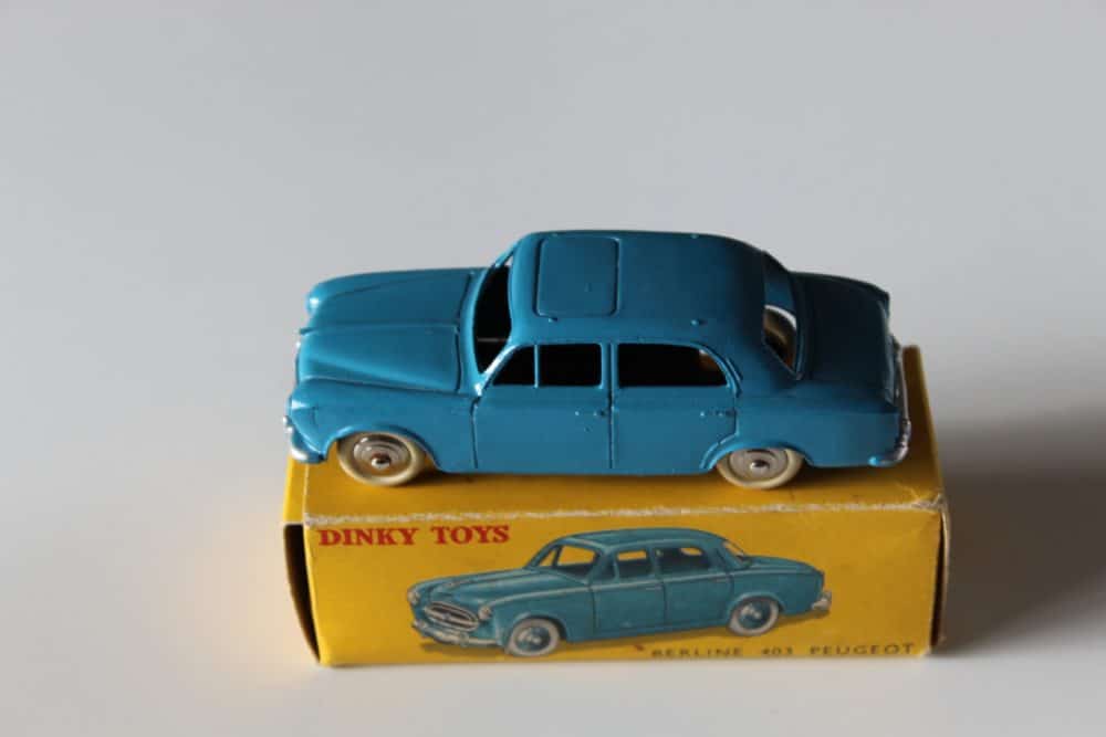 Vintage blue Dinky Toys Peugeot 403 model car on yellow box, collectible diecast vehicle.